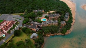 An aerial view of a coastal resort with multiple buildings, a swimming pool, and a beach. - Blue Lagoon Hotel and Conference Centre (East London)