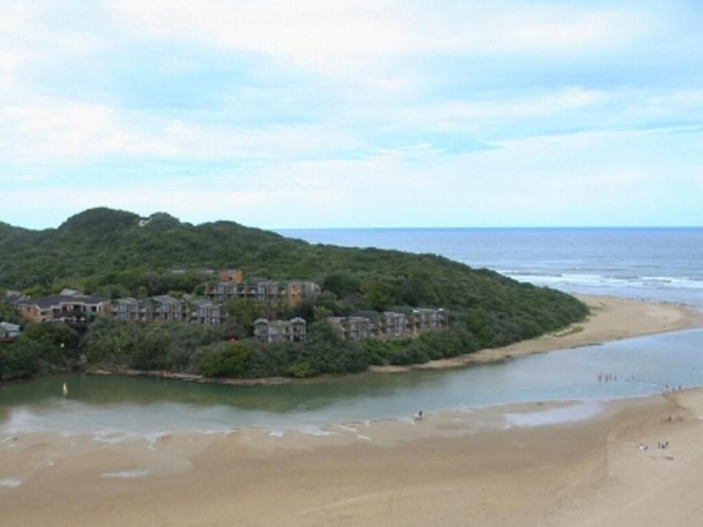 A coastal area with a beach, a river, and a hillside with buildings.