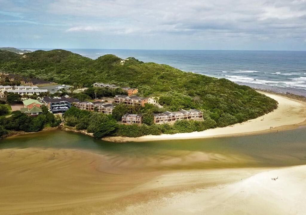 Un complejo turístico costero con varias construcciones rodeado de vegetación exuberante y una playa de arena.