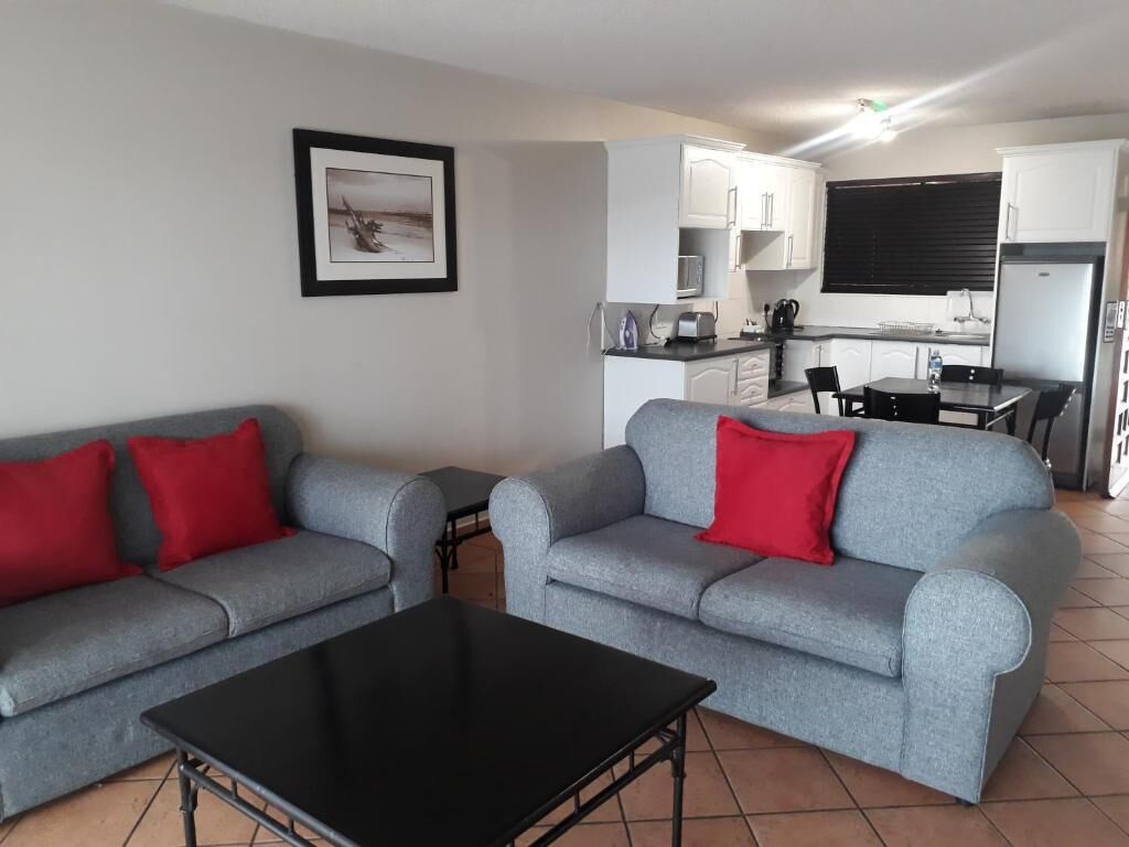 A modern living room with grey sofas and red cushions, a black coffee table, and a kitchen area in the background.