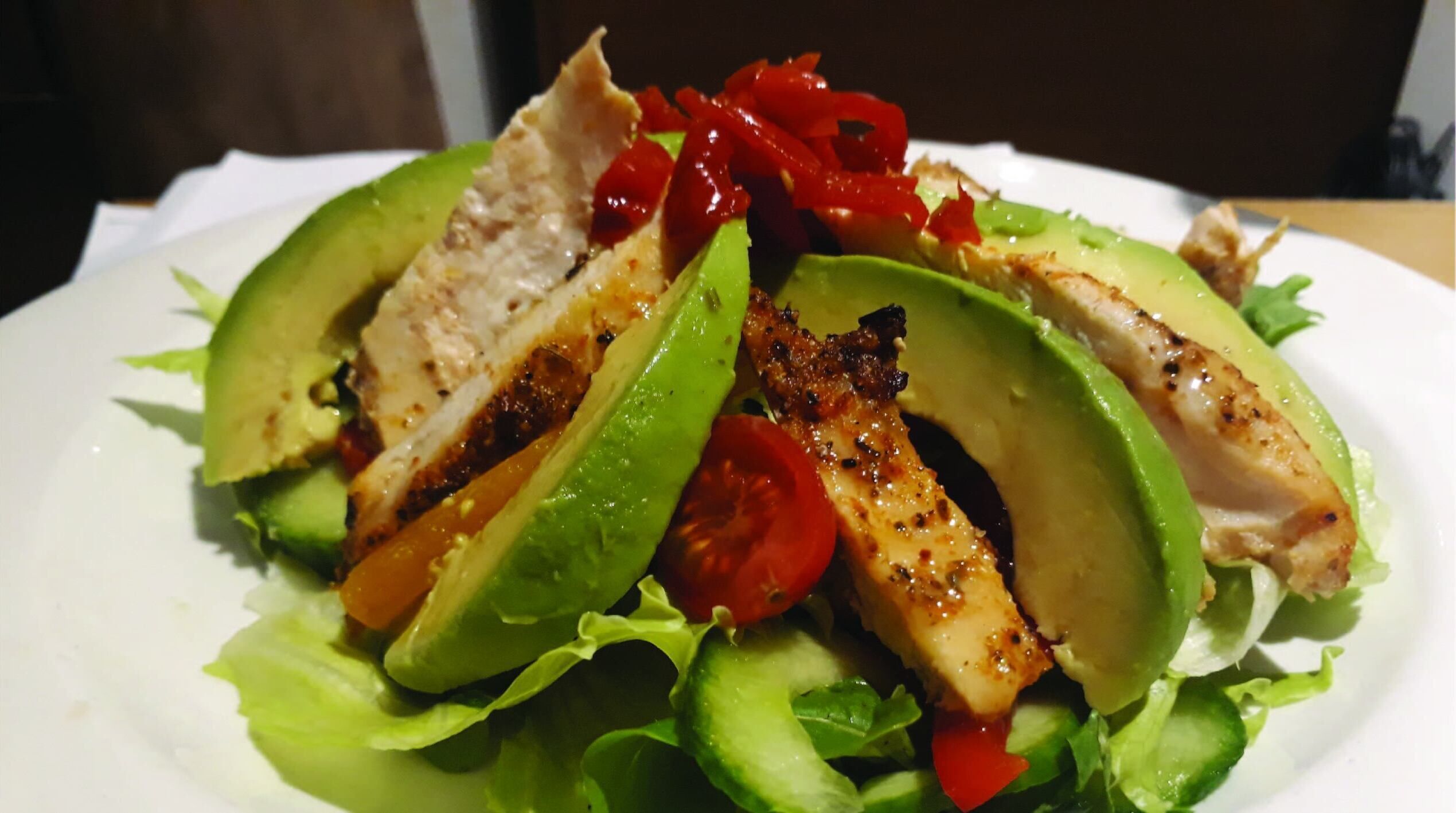 Un plato de pollo a la parrilla, rebanadas de aguacate, tomates cherry y lechuga.