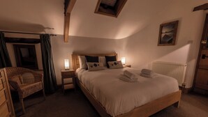A cozy bedroom with a wooden bed, a nightstand with a lamp, a wicker chair, and a radiator. - Townfoot Barn (Windermere)