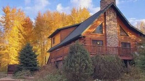 A log cabin with a stone chimney, surrounded by autumn foliage.