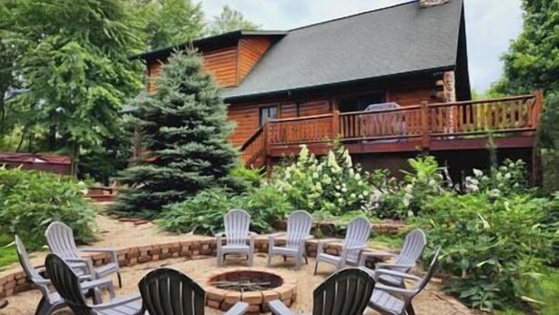 A wooden cabin with a deck and a fire pit surrounded by chairs.