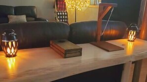 A wooden coffee table with two lit lanterns, a book, and a remote control.