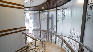 Una escalera moderna con detalles de madera y barandales de metal, que conduce a una habitación con un gran ventanal y paneles decorativos en la pared.