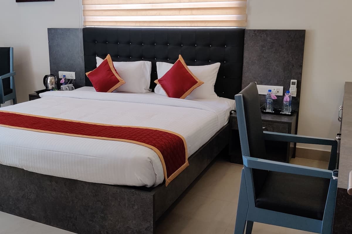 A modern hotel room with a large bed, a small round table, a chair, and a bedside table with a lamp and a phone.