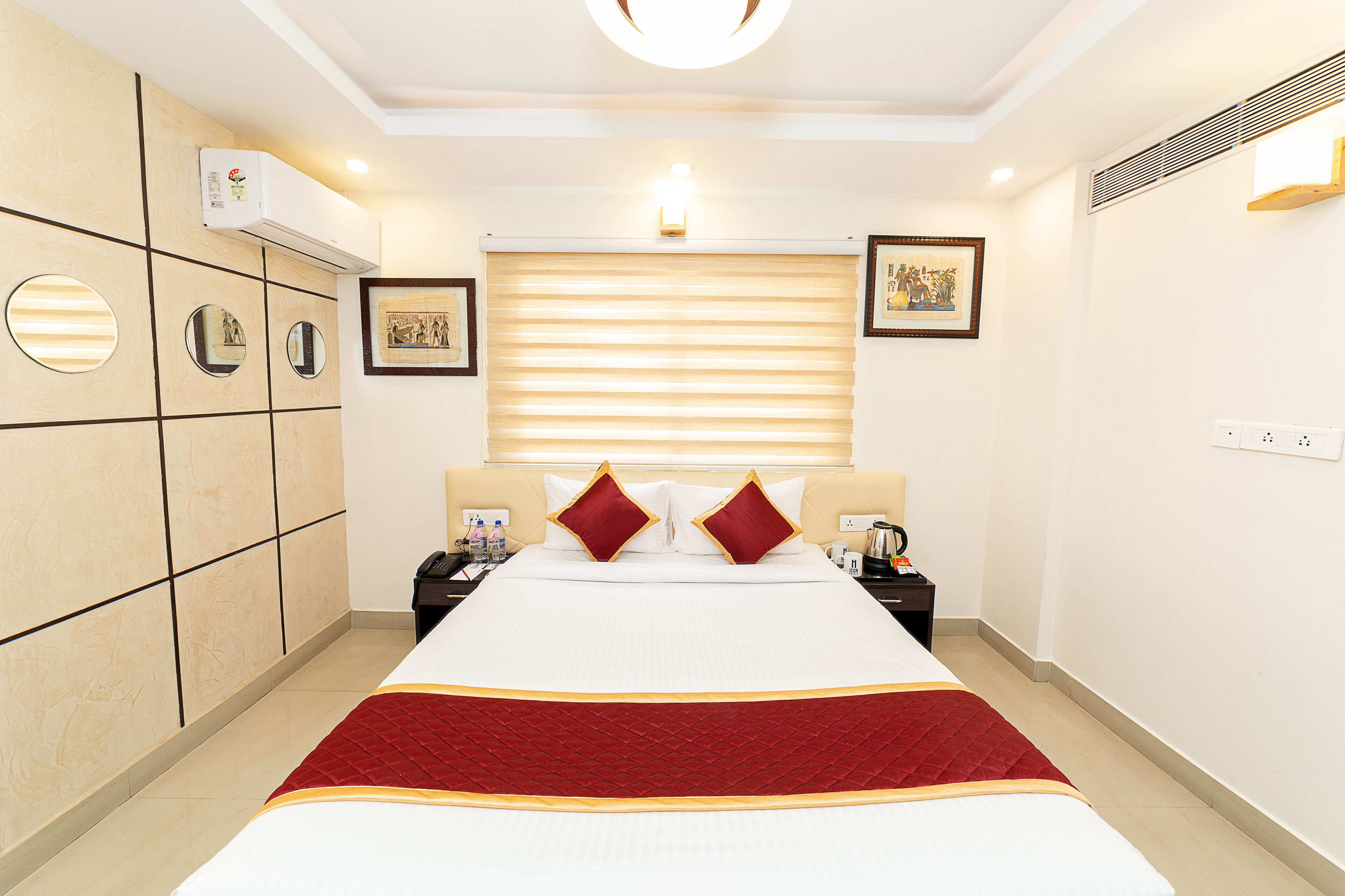 A hotel room with a large bed, a wardrobe, a bedside table with a lamp, and a window with blinds.