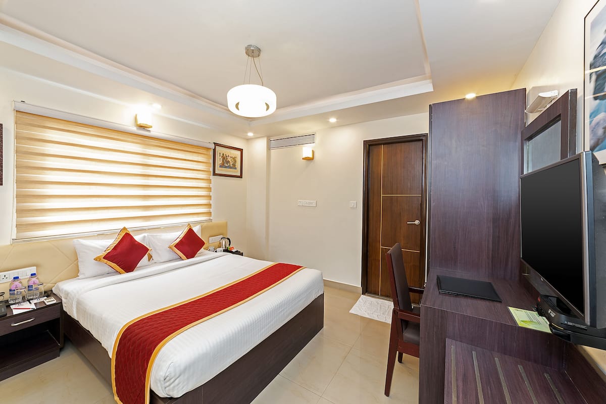 A hotel room with a bed, bedside table, TV, and a desk with a chair.