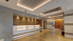 Un área de recepción moderna con un mostrador de madera, un muro con motivo de espiga y una escalera de mármol.