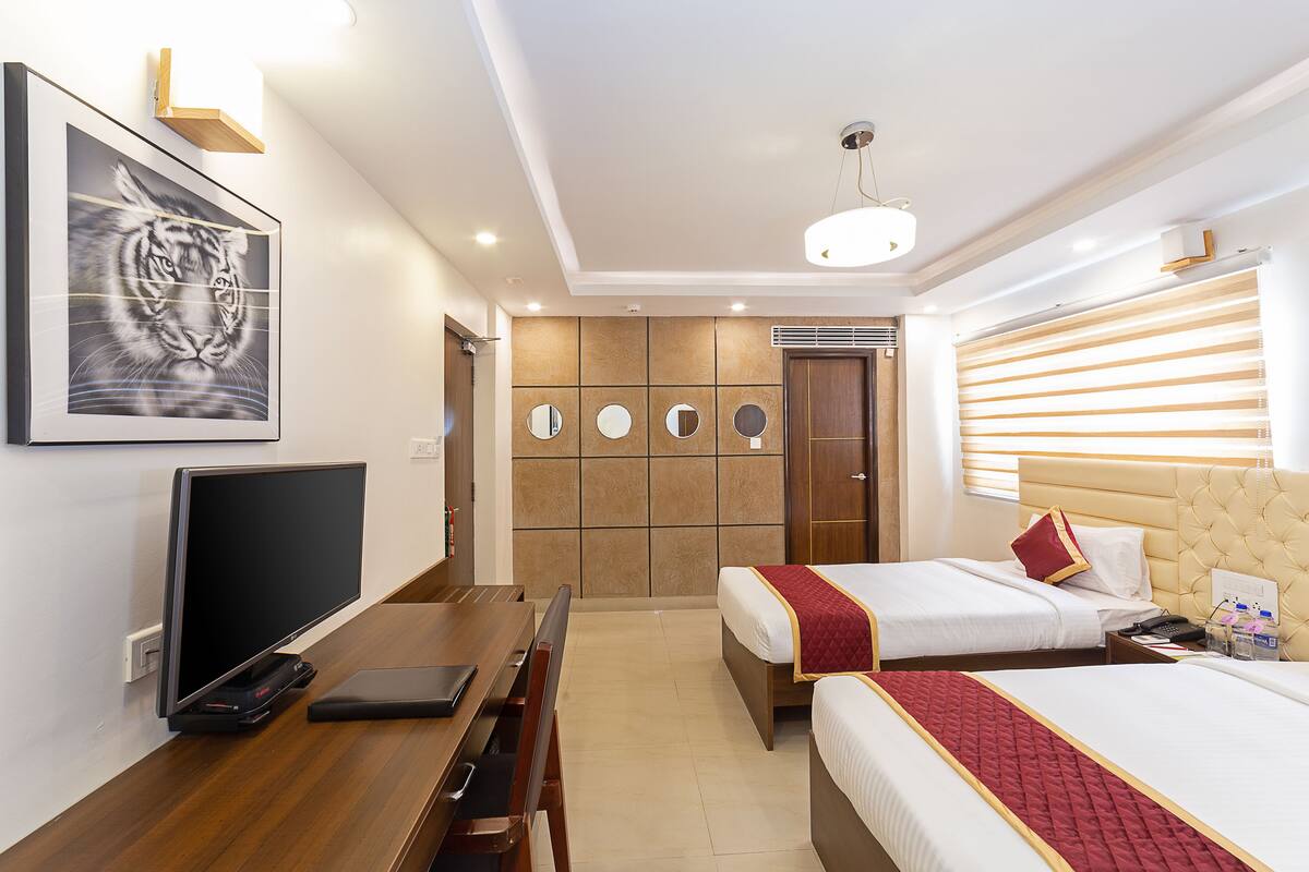 A hotel room with two beds, a desk, a TV, and a wall-mounted artwork.
