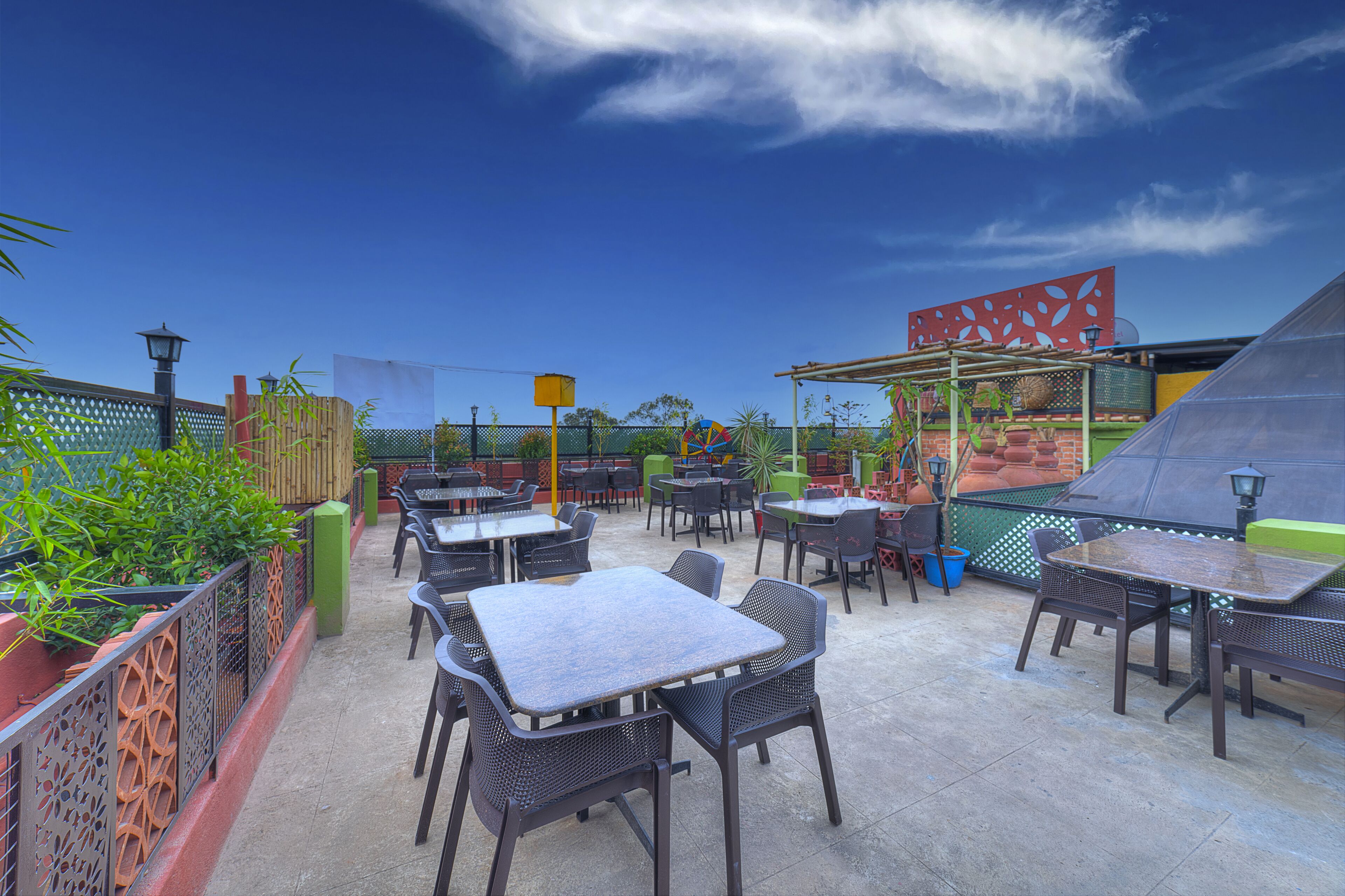 An outdoor patio with multiple tables and chairs, surrounded by a decorative fence and potted plants.