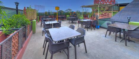 An outdoor patio with multiple tables and chairs, surrounded by a decorative fence and potted plants.