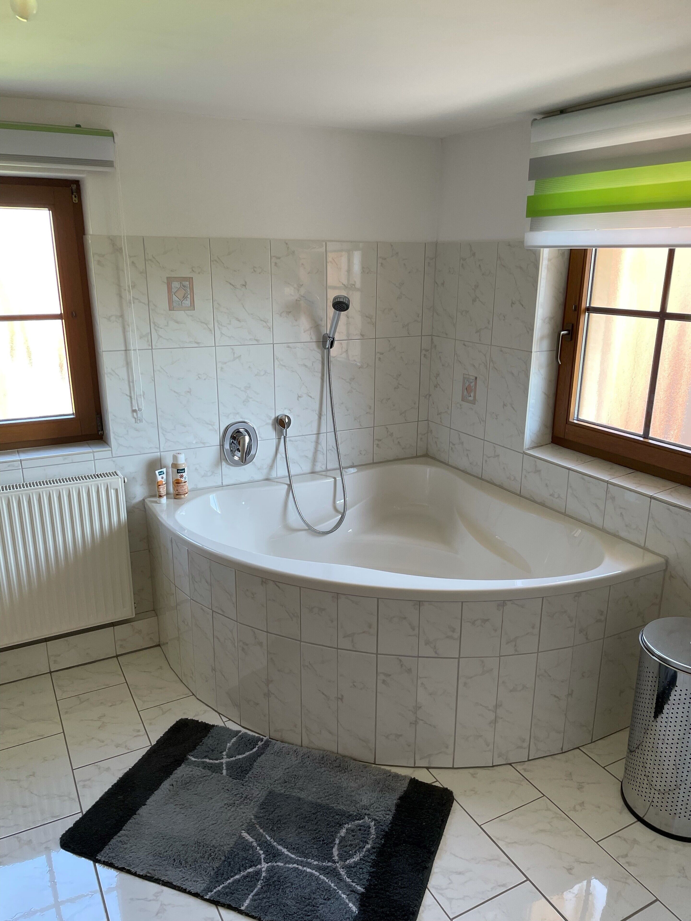 A bathroom with a freestanding bathtub, a window, a radiator, and a trash can.