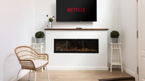Una sala moderna con una televisión de pantalla plana sobre la chimenea, un sillón de mimbre y dos mesitas auxiliares con plantas en macetas.