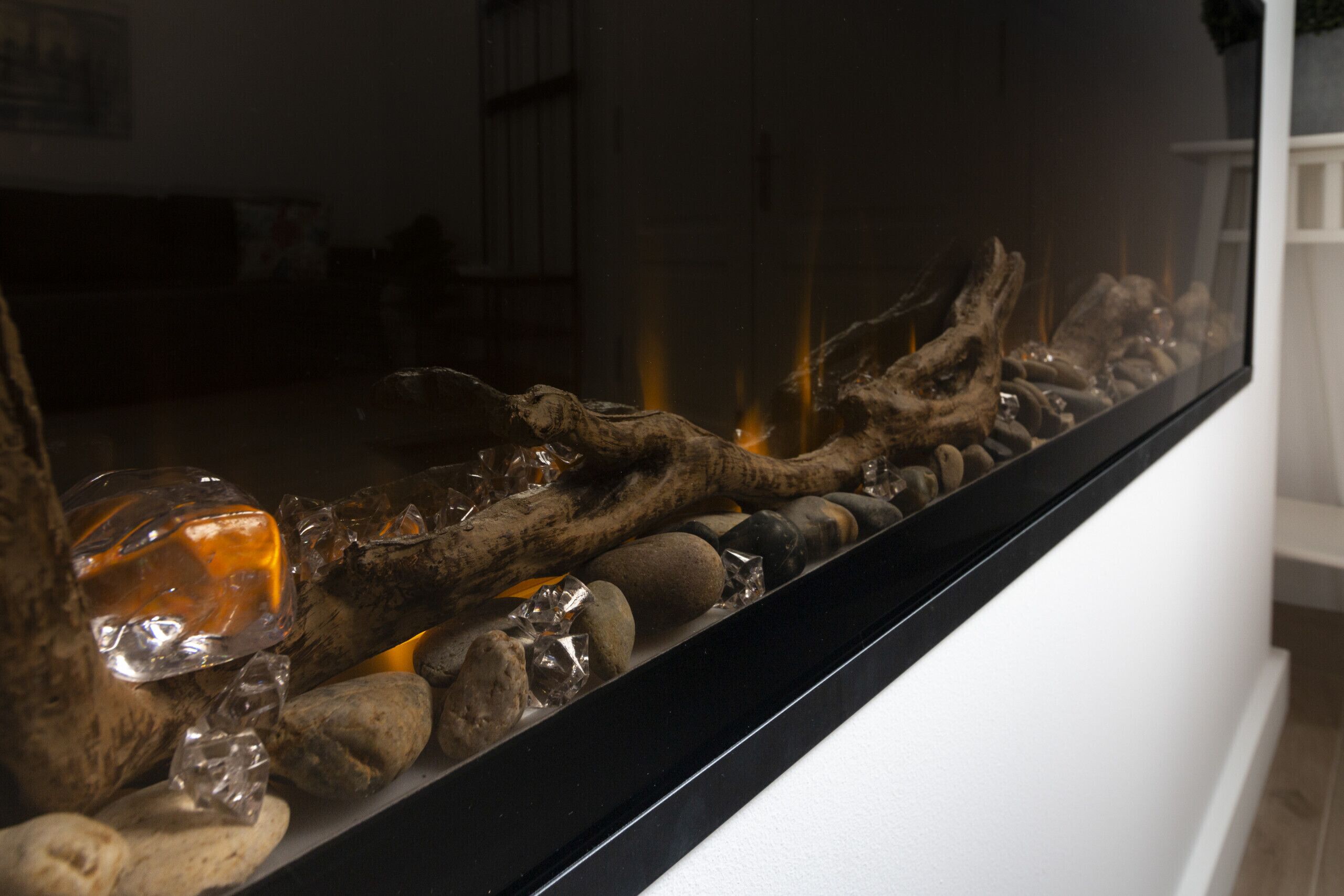 A decorative glass piece with a reflective surface, surrounded by smooth stones and a piece of driftwood.