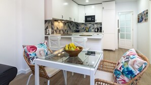 Una cocina moderna con armarios blancos, microondas y comedor con sillas de mimbre y mesa de vidrio.