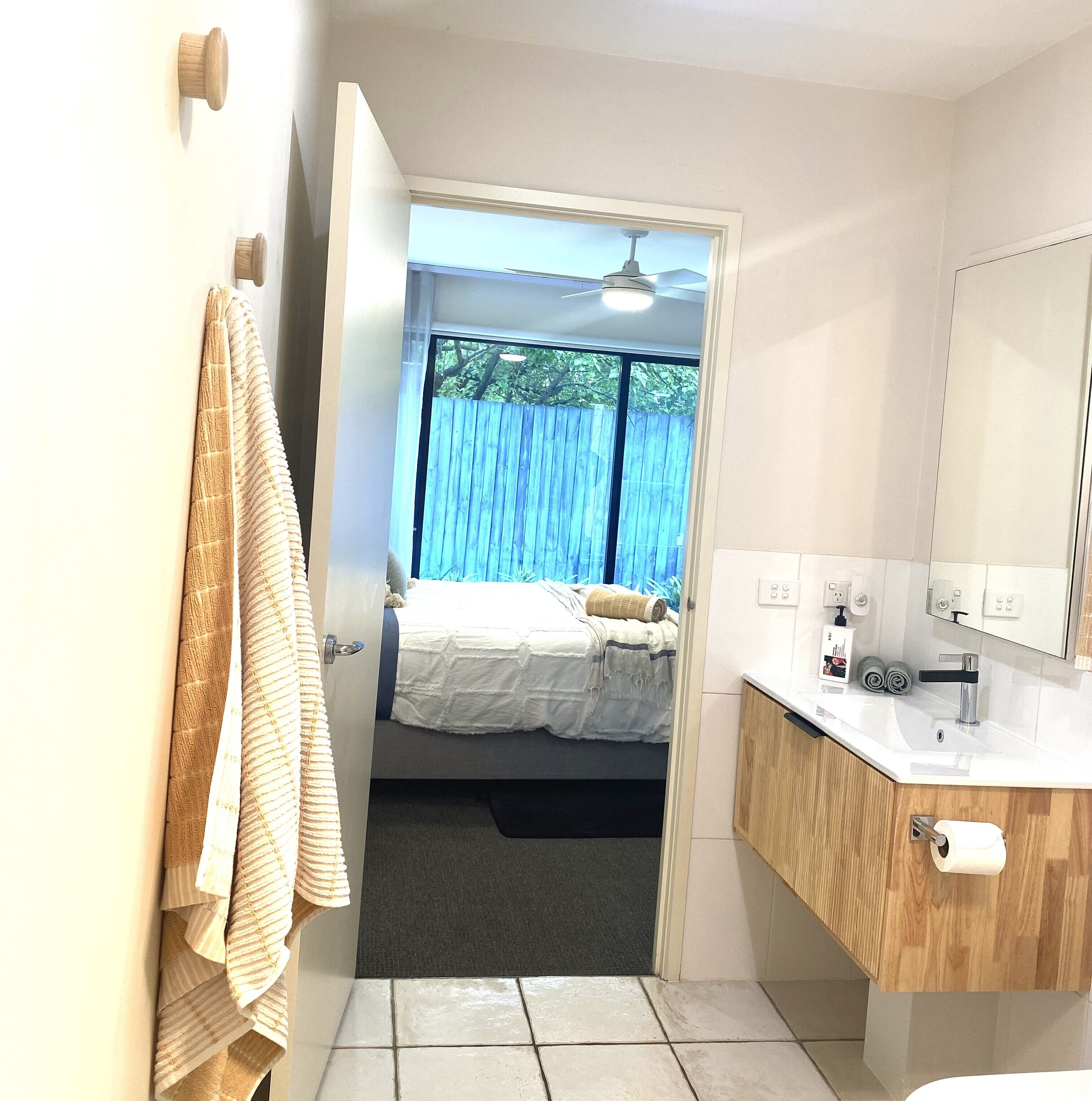 A bedroom with a bed, a window with a view of trees, and a bathroom with a sink and mirror.