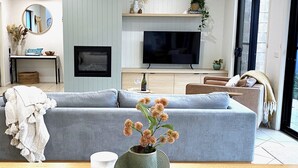 Un salon moderne avec un canapé gris, une table basse en bois agrémentée d’objets décoratifs, un téléviseur et une grande fenêtre.