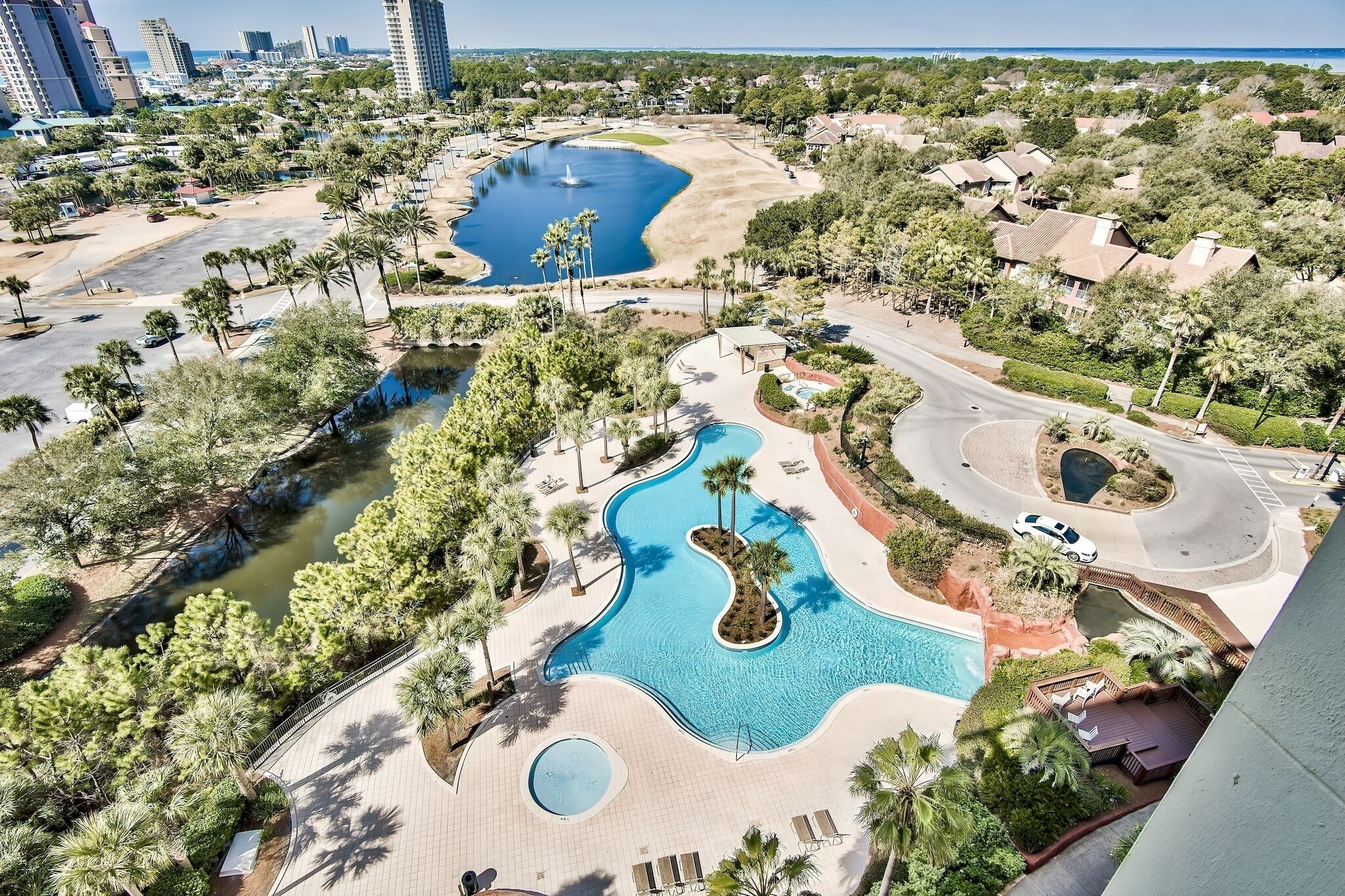 Vista aérea de un resort con una amplia piscina, palmeras y un lago.