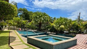 Zona de piscina con varios jacuzzis, rodeada de palmeras y un solárium empedrado.