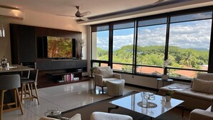 Una sala de estar moderna con un televisor grande, asientos cómodos, una zona de comedor y vistas a abundante vegetación.