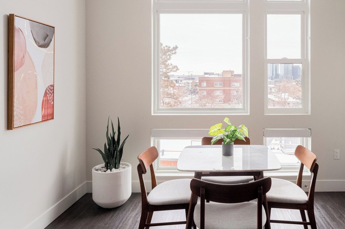 A dining area with a table and chairs, a potted plant, and a window with a view of buildings.