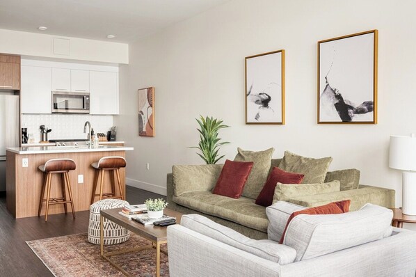 A modern living space with a kitchen island, bar stools, a sofa set, and two framed artworks on the wall.
