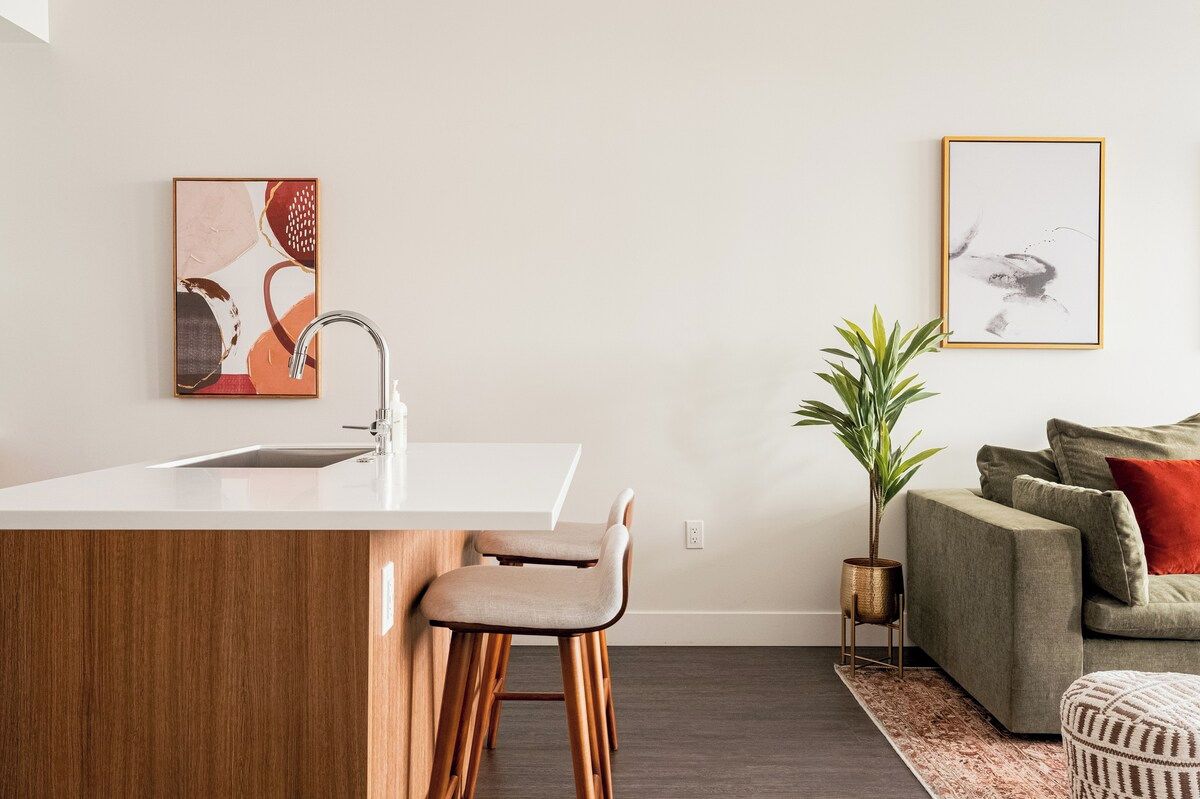A modern kitchen with a white countertop, stainless steel sink, and wooden stools.