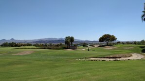 Un campo da golf con cielo sereno, montagne in lontananza e alcuni alberi.