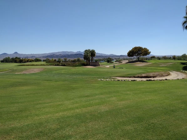 A golf course with a clear sky, distant mountains, and a few trees.