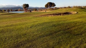 Un campo da golf con uno stagno, alberi e montagne in lontananza.