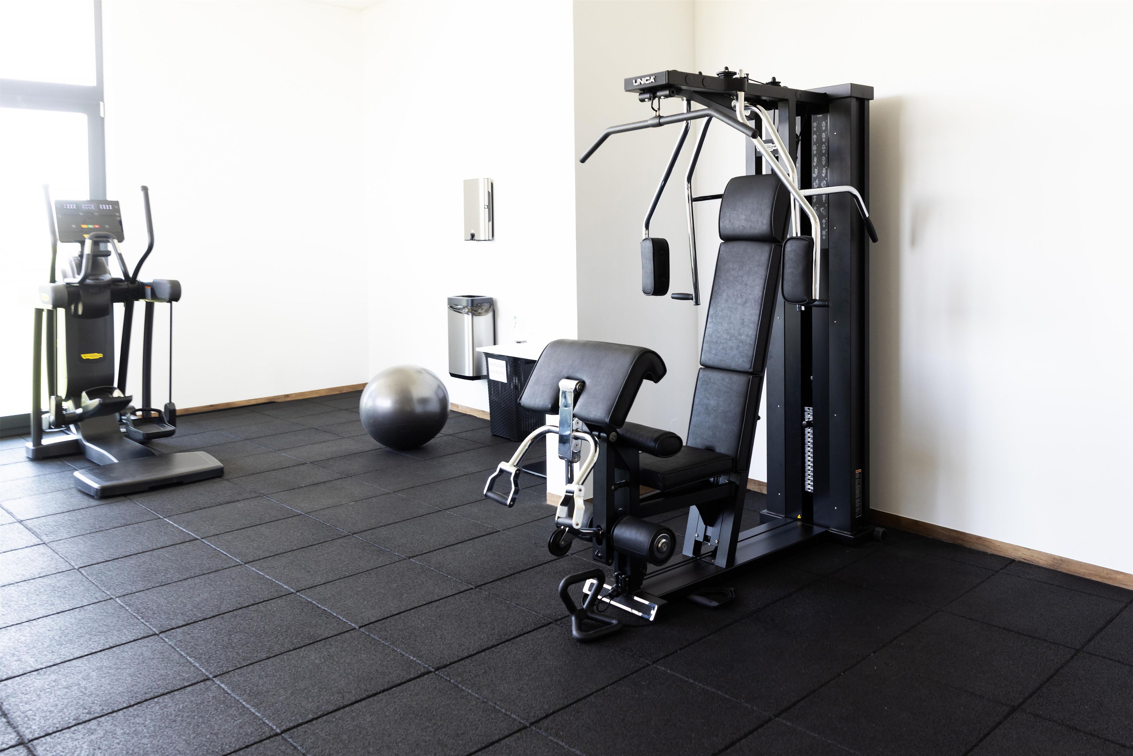 Une salle de sport équipée de matériel d’exercice, d’un banc de musculation, d’un ballon lesté et d’un support à squats fixé au mur.