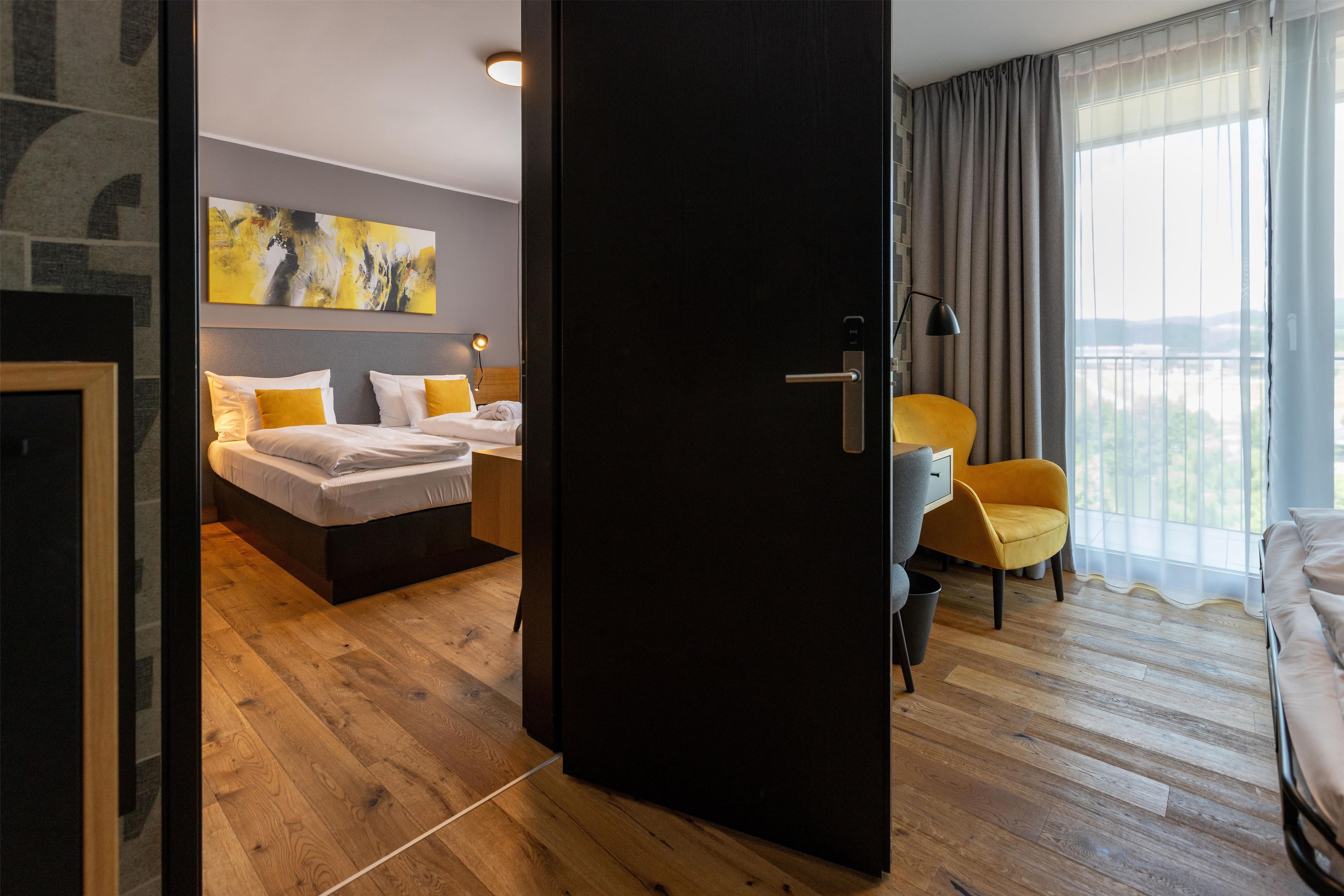 A hotel room with a bed, a desk, a chair, and a large window.
