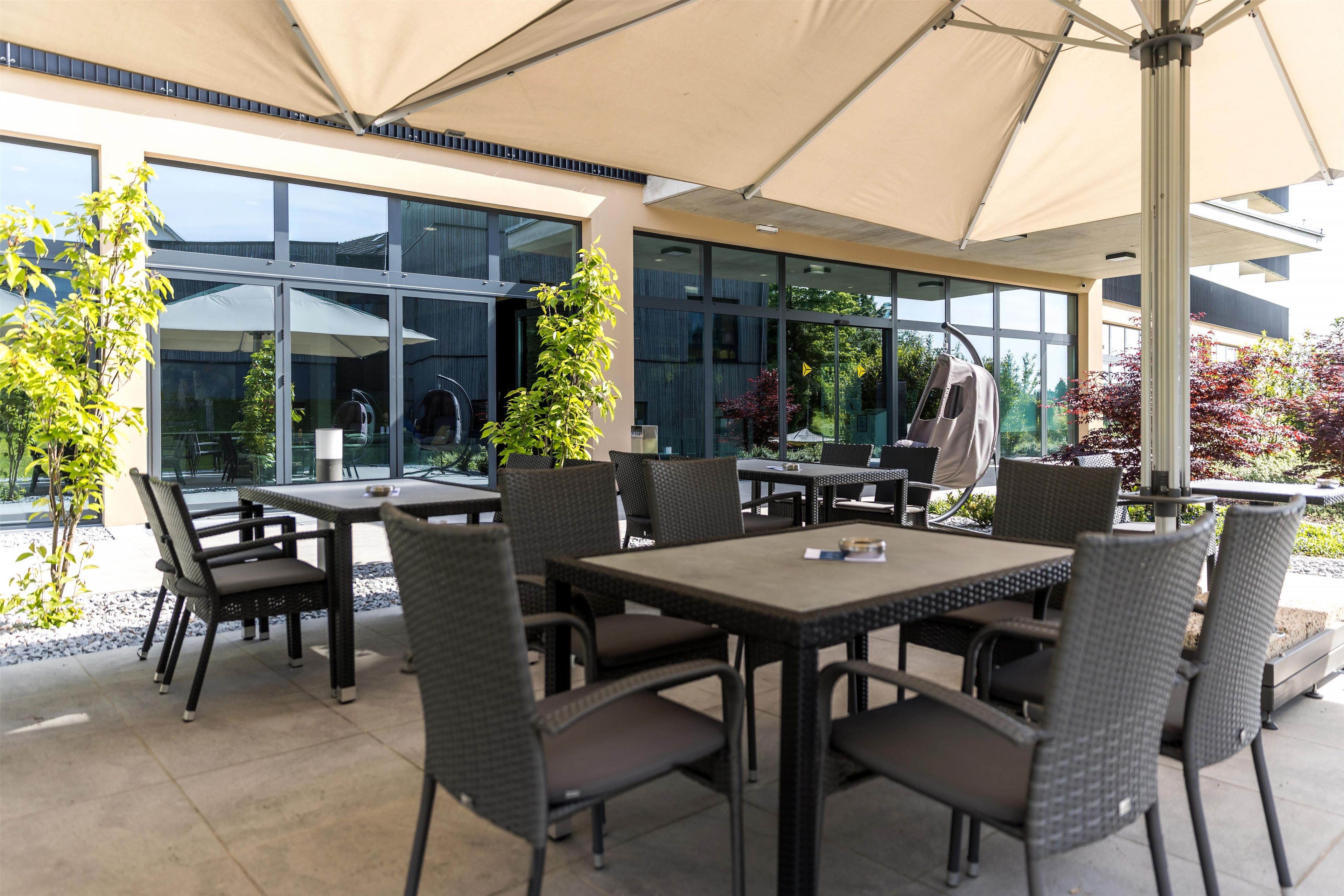 An outdoor seating area with tables and chairs, large windows, and a covered section.