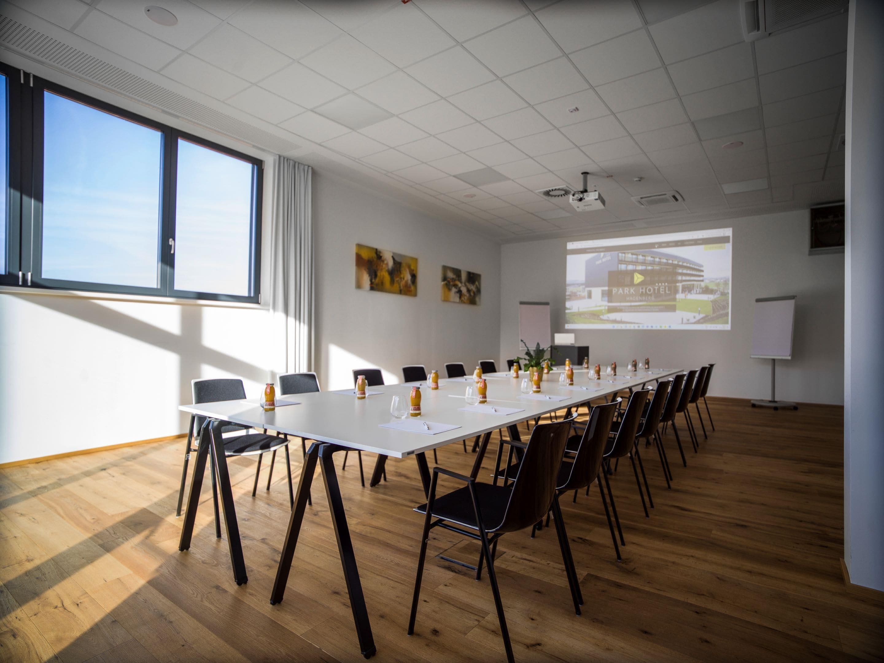 A conference room with a long table, chairs, a projector screen, and a whiteboard.