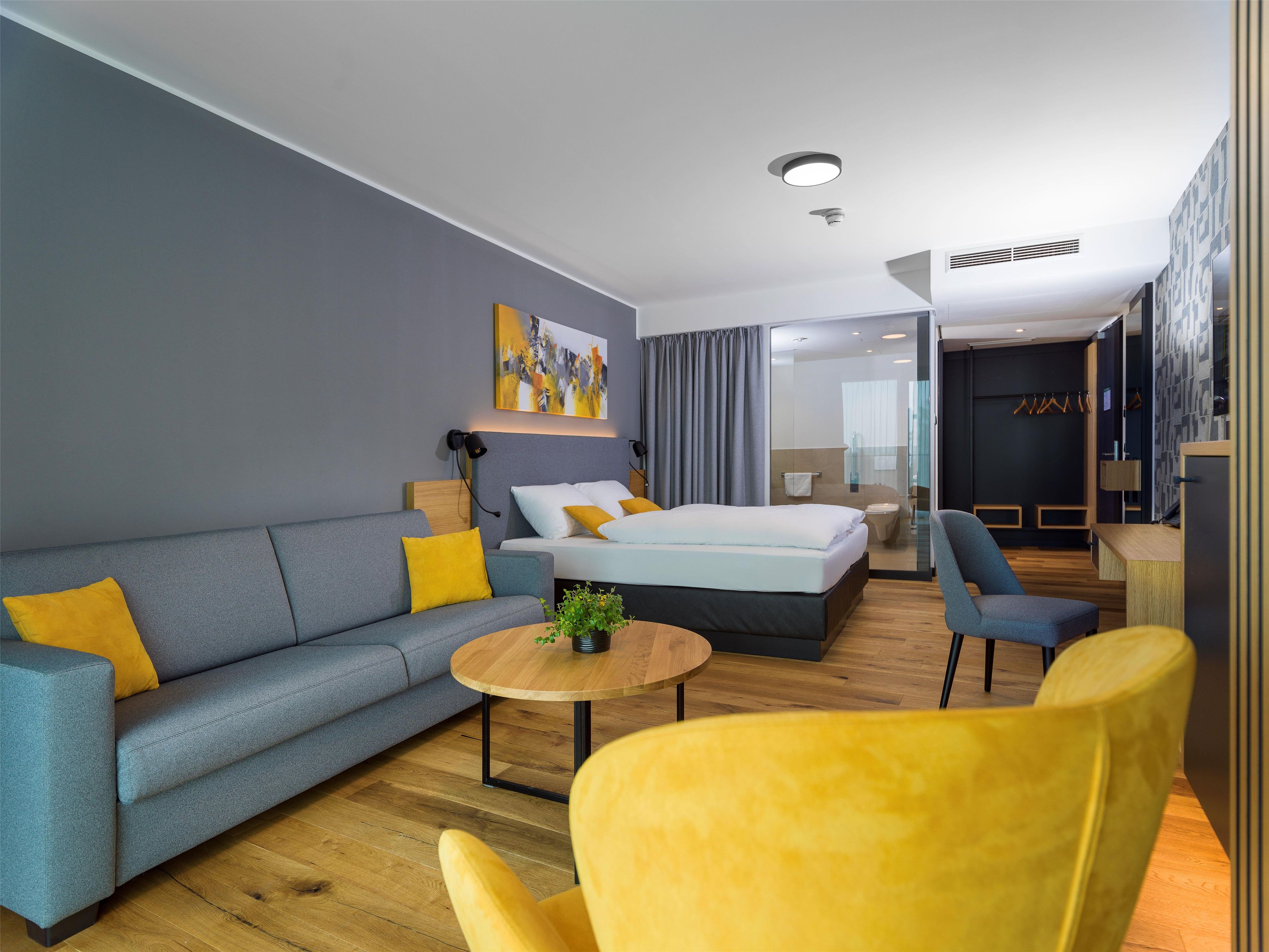 A modern hotel room with a sofa, a bed, a small table, and a chair.