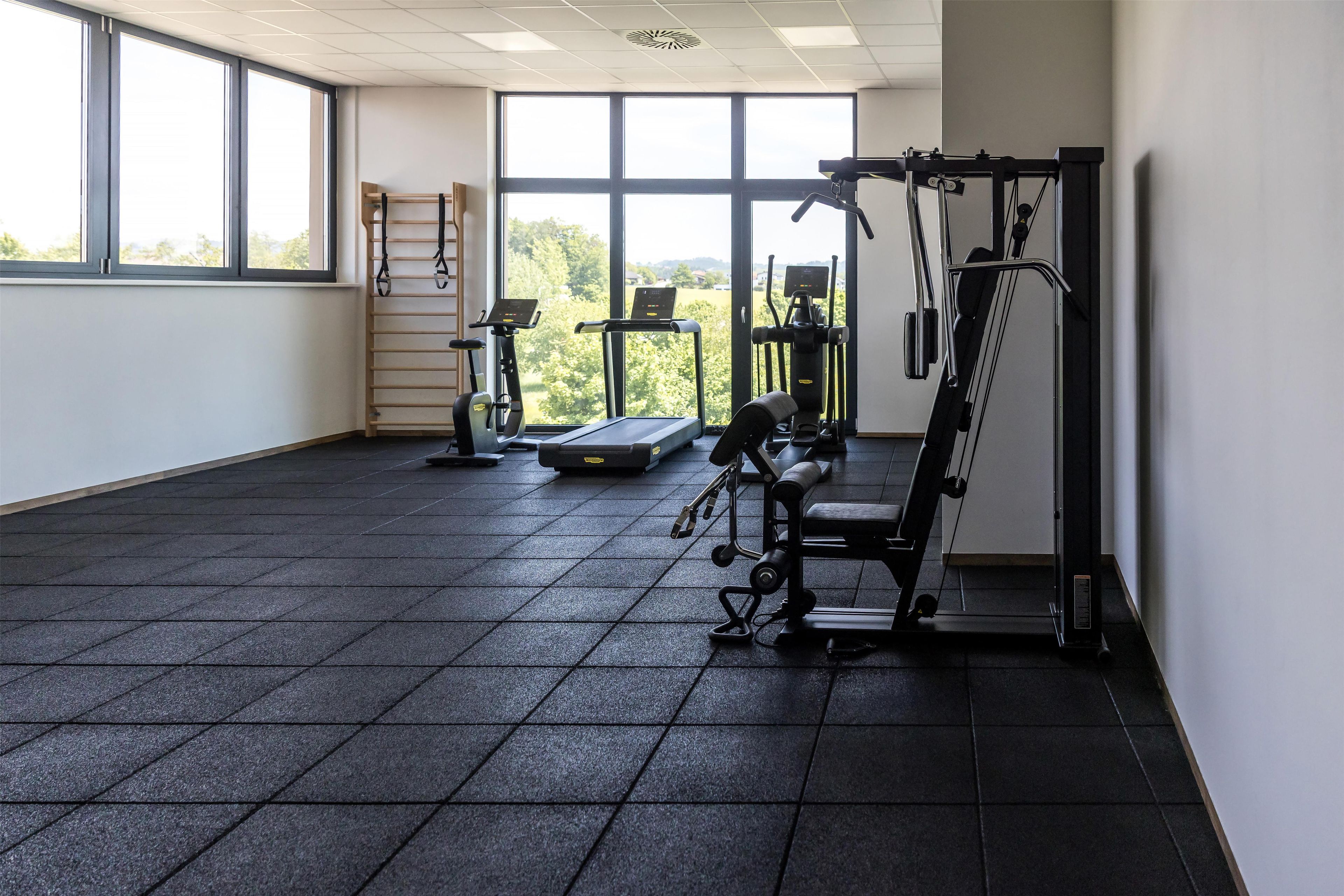 A gym with exercise equipment, a treadmill, and a view of trees through large windows.