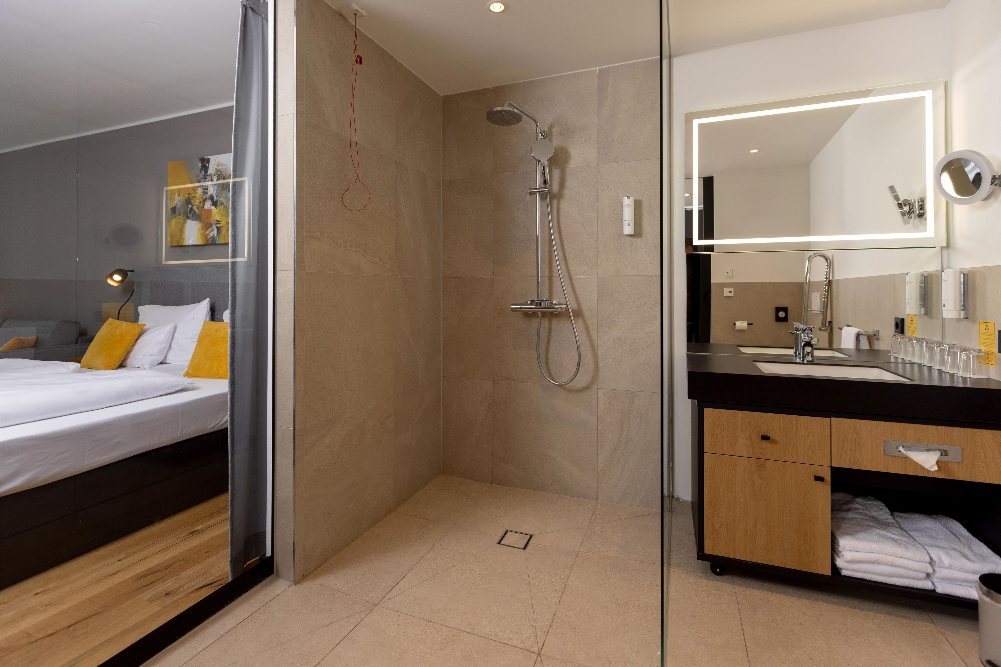 A modern bathroom with a shower, a vanity with a mirror, and a bed with a headboard.