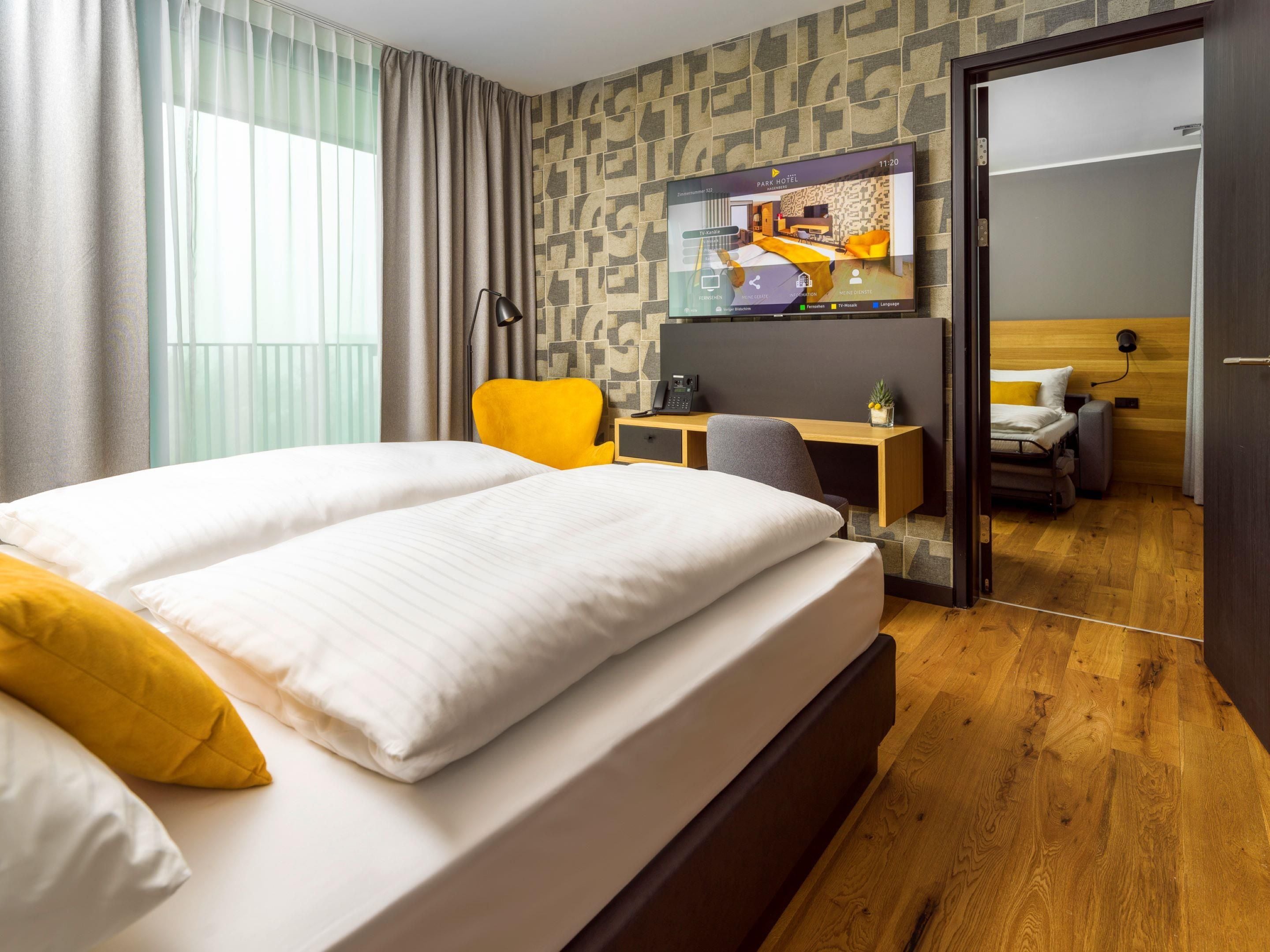 Une chambre d’hôtel avec un lit, un bureau, une chaise et une vue sur une autre chambre.