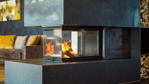 A modern fireplace with a glass enclosure, a dark-toned wall, and a stack of firewood to the right. - Best Western Parkhotel Hagenberg (Hagenberg im Mühlkreis)