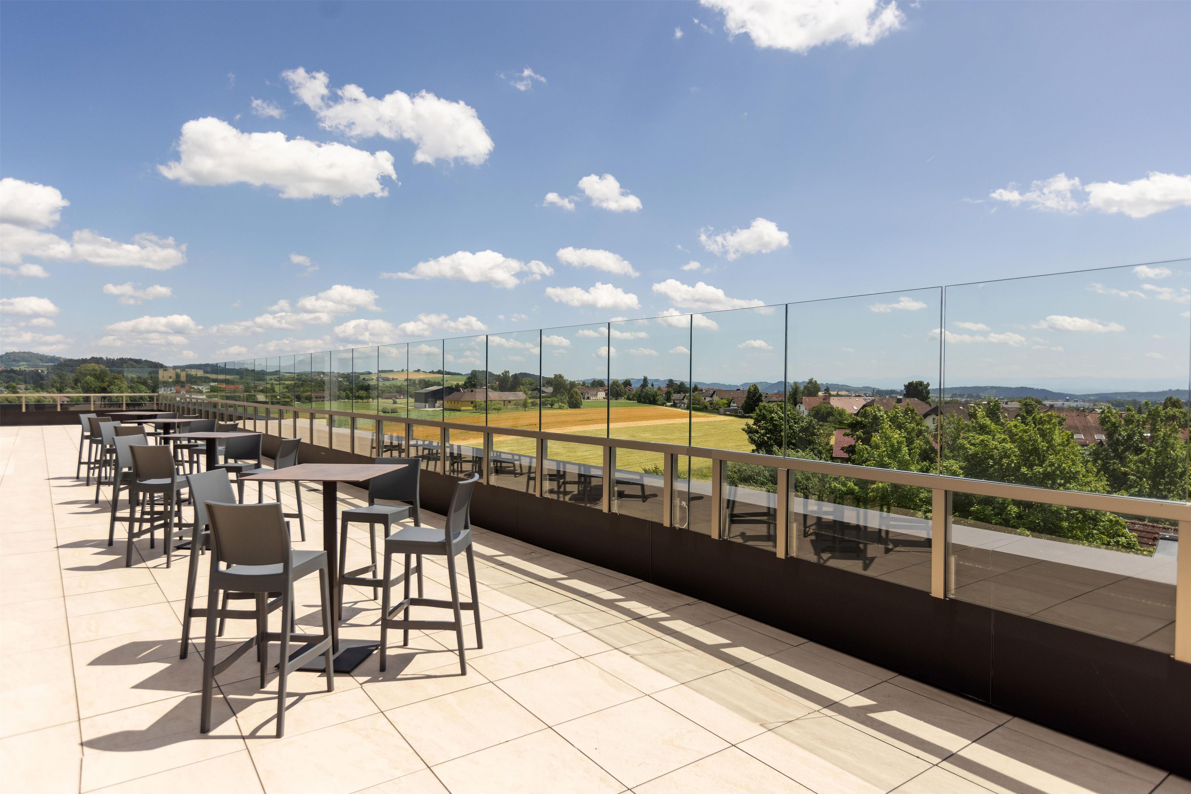 Una terraza con mobiliario exterior y vistas a un campo y edificios al fondo.