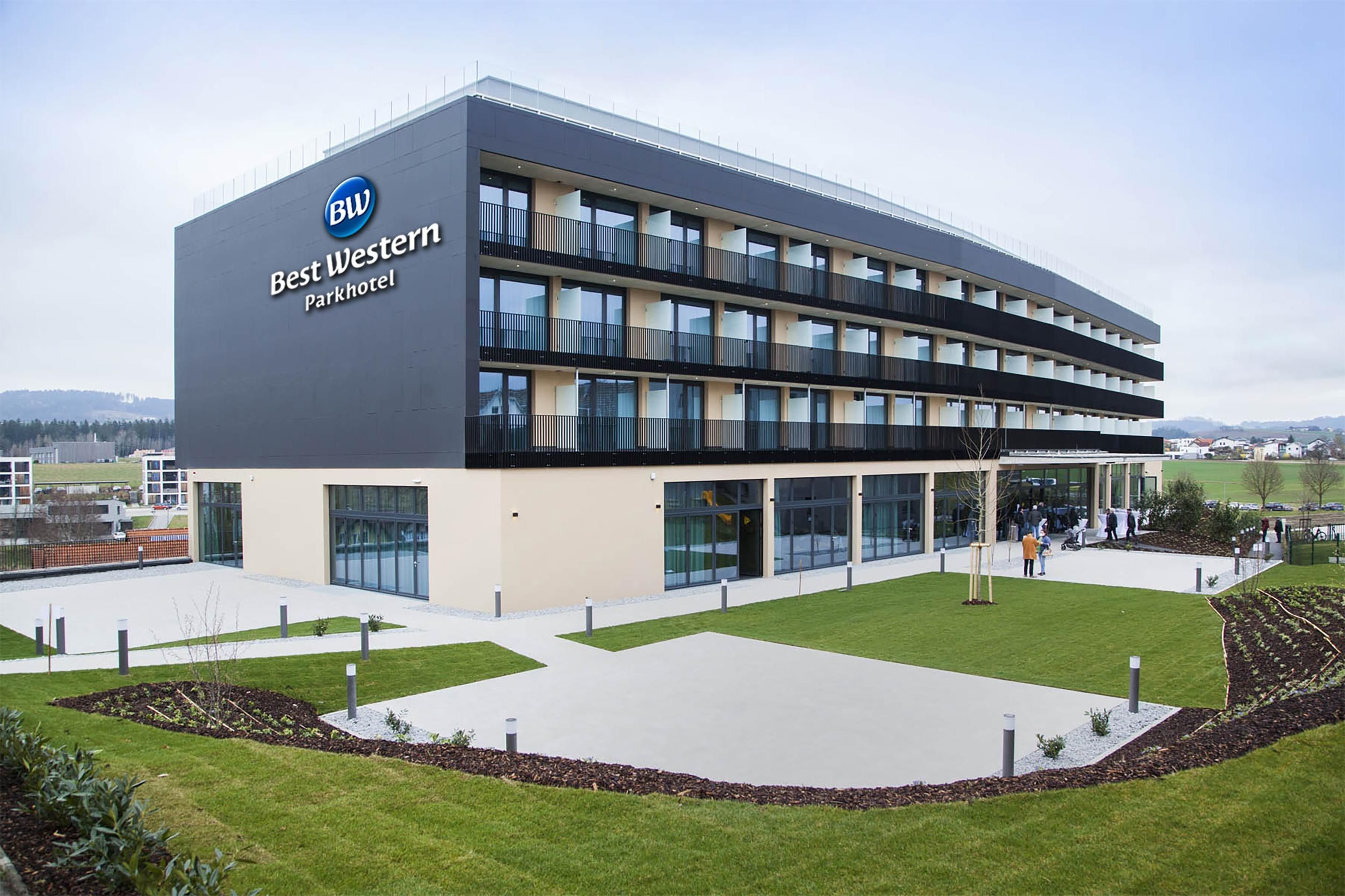 Un moderno Best Western Parkhotel con estructura de varios pisos, grandes ventanales y un área exterior bien cuidada con senderos y vegetación.