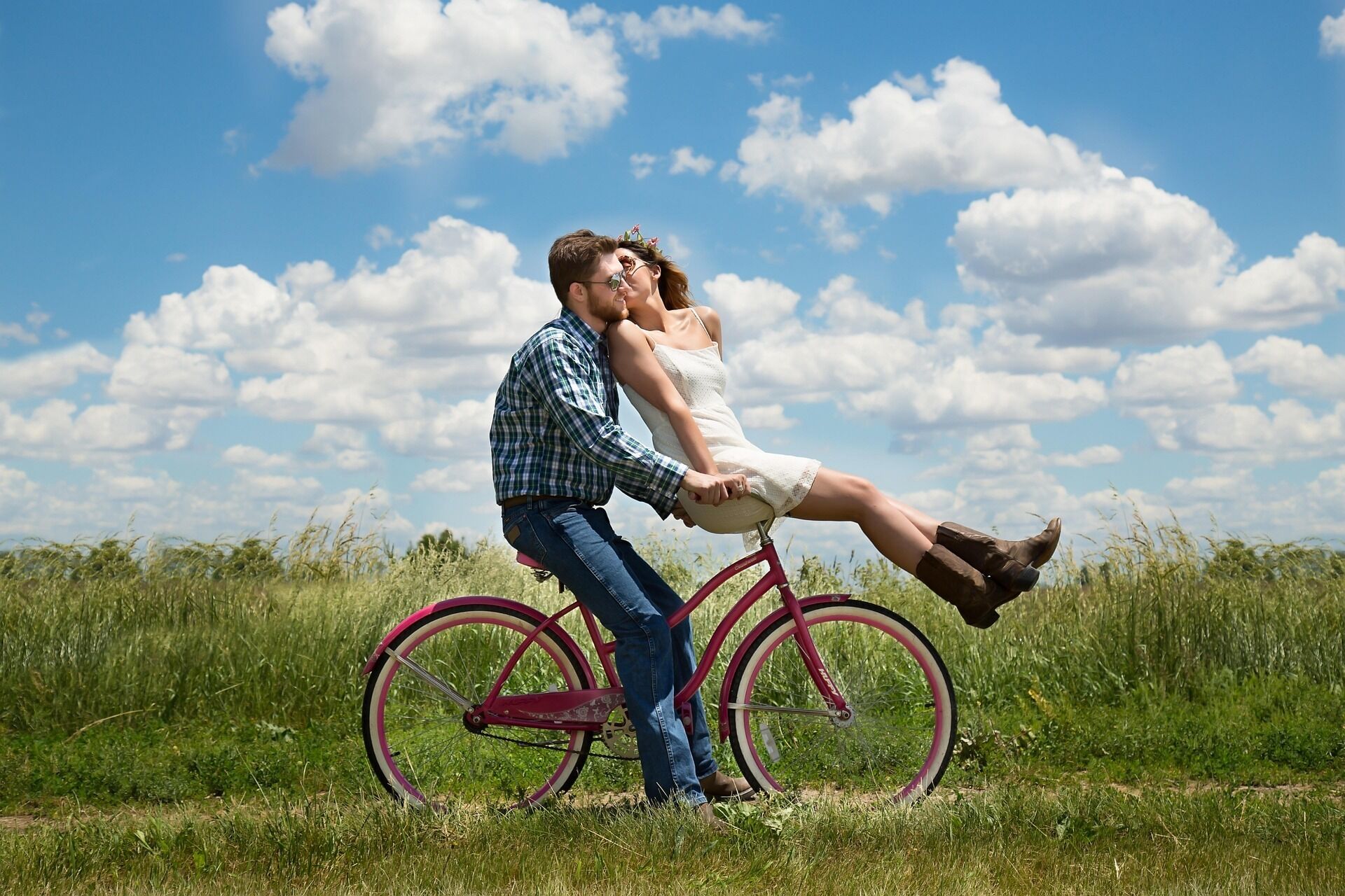 Un couple à vélo dans un champ verdoyant, sous un ciel dégagé.