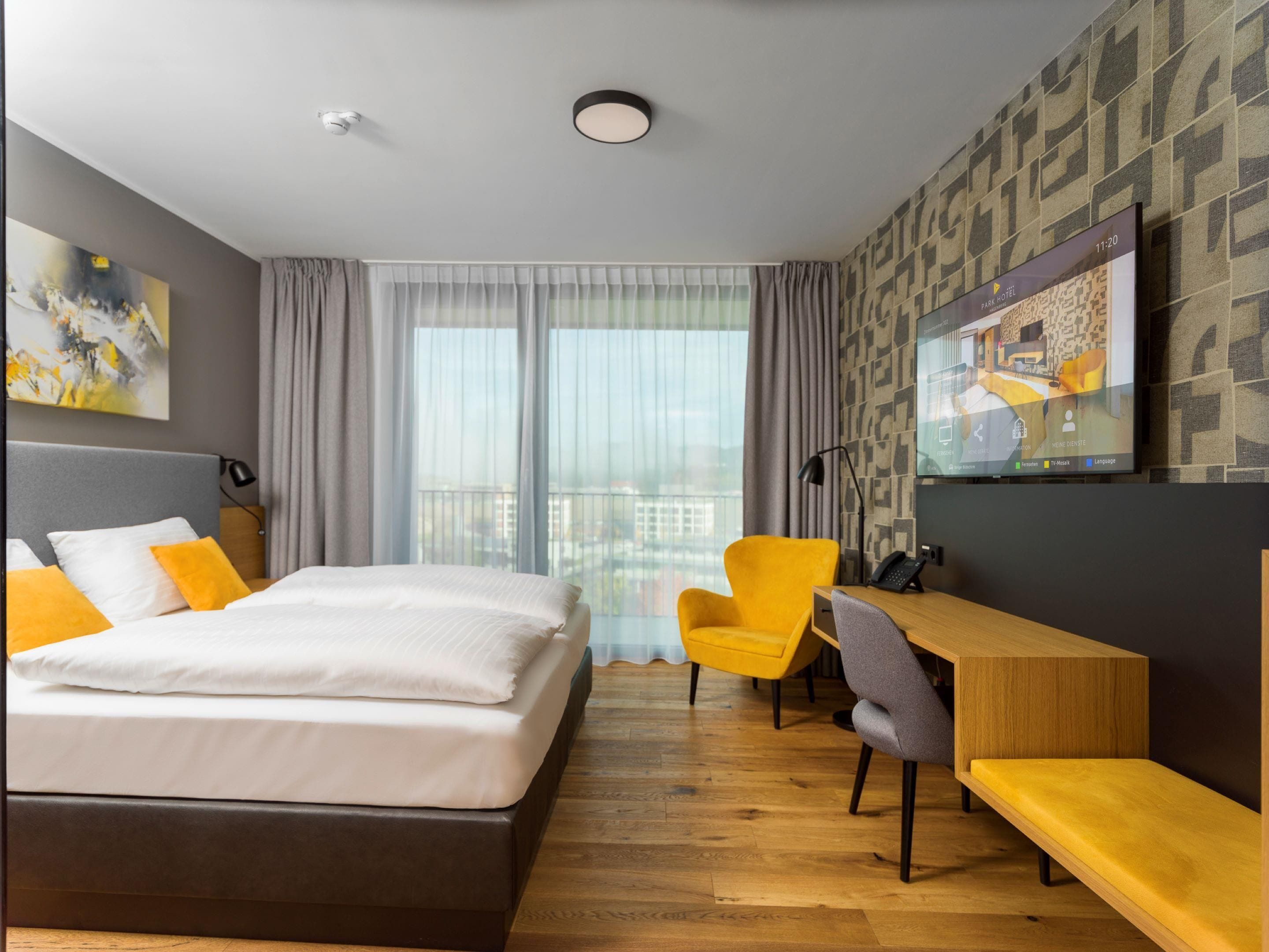 A hotel room with a bed, a desk, a chair, a TV, and a view of the city.
