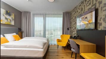 Habitación de hotel con cama, escritorio, silla, televisor y vista a la ciudad.