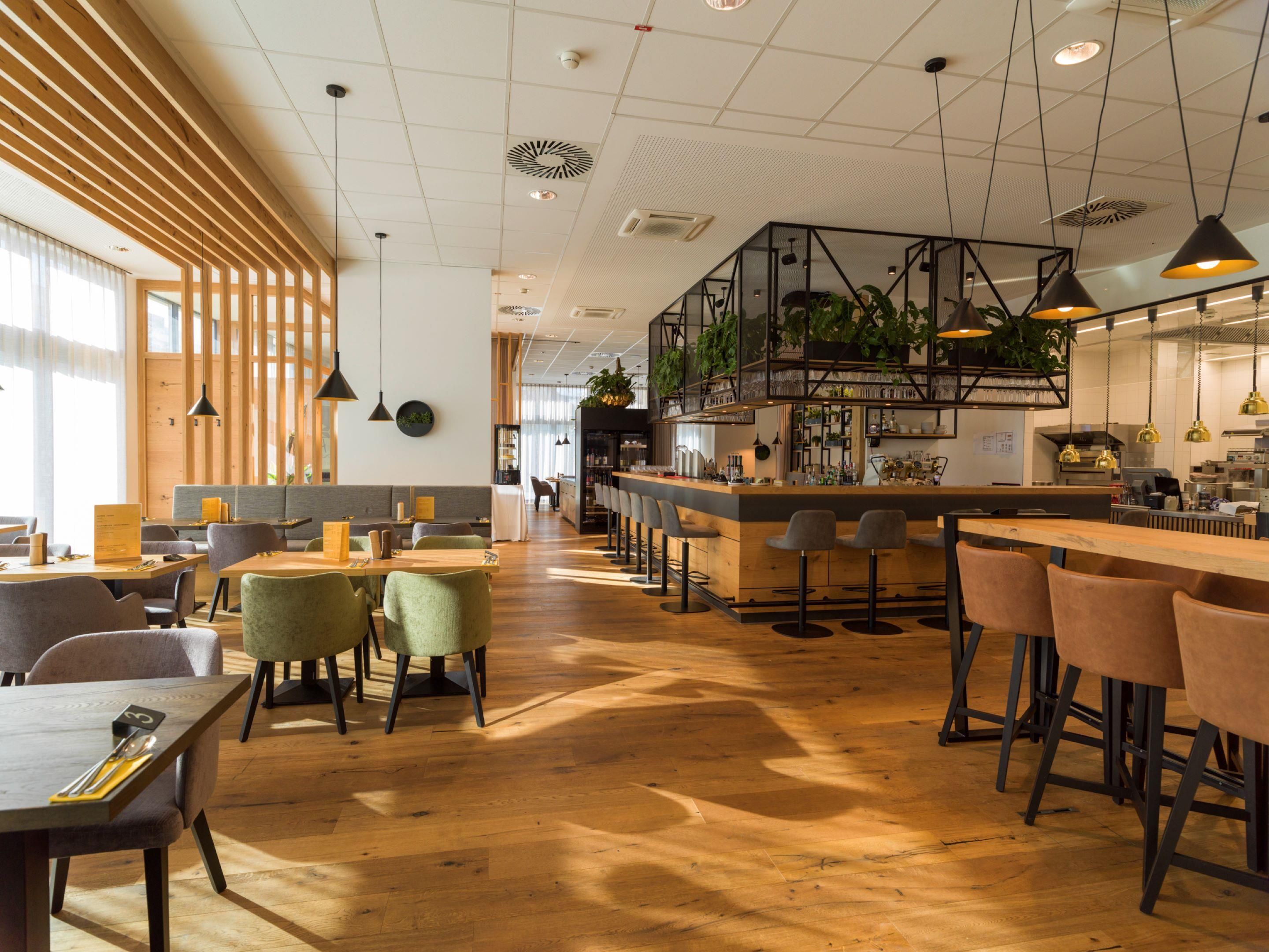 A modern interior with a wooden floor, bar area, seating, and a kitchen visible in the background.