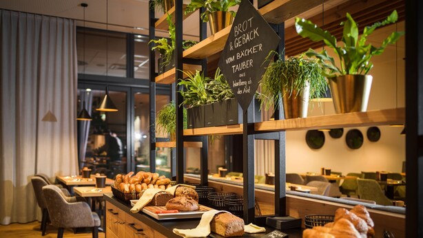 A bakery counter with various breads and pastries, wooden furniture, and potted plants. - Best Western Parkhotel Hagenberg (Hagenberg im Mühlkreis)