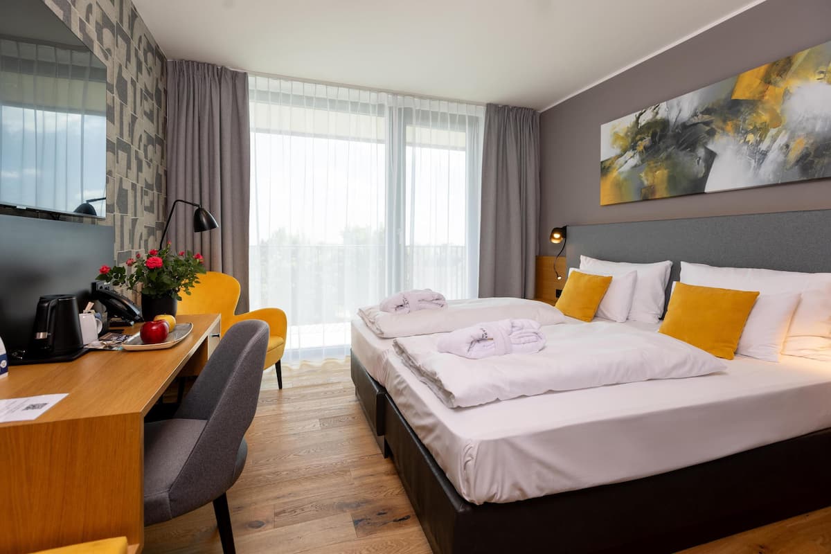 Ein Hotelzimmer mit Bett, Schreibtisch, Stuhl und einem großen Fenster mit Vorhängen.