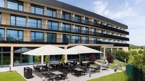A modern building with multiple balconies, outdoor seating with umbrellas, and a well-maintained garden area. - Best Western Parkhotel Hagenberg (Hagenberg im Mühlkreis)